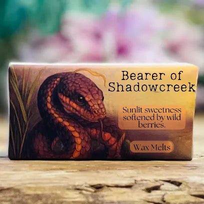 A close-up of the “Bearer of Shadowcreek” wax melt packaging with warm earthy tones and a magickal woodland feel.