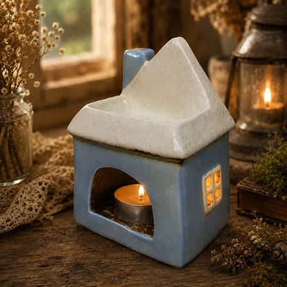 Blue ceramic cottage wax melt burner and tea light holder with warm light glowing through the windows.