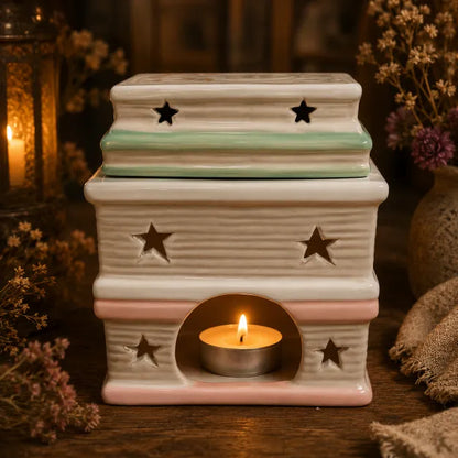 “Book Stack ceramic wax melt burner in cream, blush pink and mint green, with star cut-outs and a lit tea light inside.”