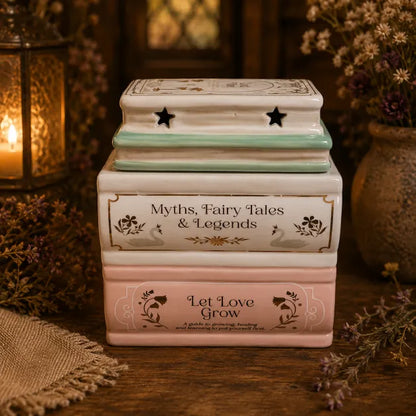 “Ceramic Book Stack wax melt burner in cream, blush pink and mint green, featuring Myths, Fairy Tales & Legends and Let Love Grow designs.”