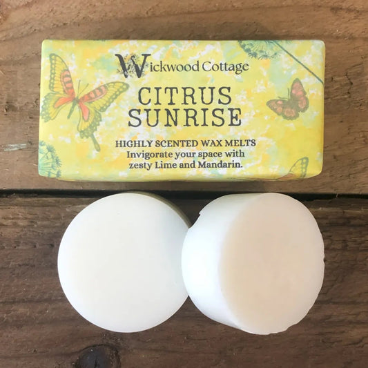 Wickwood Cottage “Citrus Sunrise” wax melt packaging displayed on a rustic wooden surface, featuring butterfly artwork and bright yellow tones, with other Wickwood wax melts softly blurred in the background.