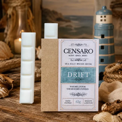 Censaro Drift sea salt wood-musk wax melts in a kraft paper sleeve with a white label, displayed alongside two white wax melts on a rustic wooden surface with nautical props including a lighthouse figurine and seashells.