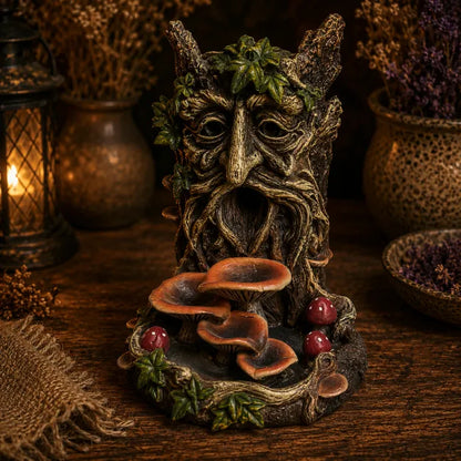 A fantasy tree spirit fountain sculpture featuring a carved forest face with leafy hair and a mouth made of mushrooms, set on a rustic wooden surface with warm, atmospheric background decor.
