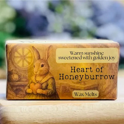 A close-up of the “Heart of Honeyburrow” wax melt packaging with warm, joyful cottagecore imagery.