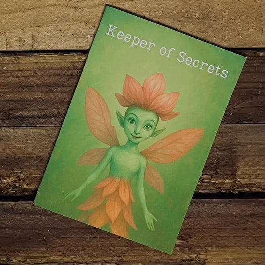 A Keeper of Secrets A5 notebook resting on a rustic wooden surface. The cover features Petalune, a green fairy with pink petal wings and a flower crown, smiling gently against a soft green background. The title ‘Keeper of Secrets’ appears at the top in white lettering