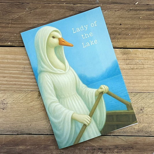 Card with a swan dressed in white titled 'Lady of the Lake' on a wooden surface