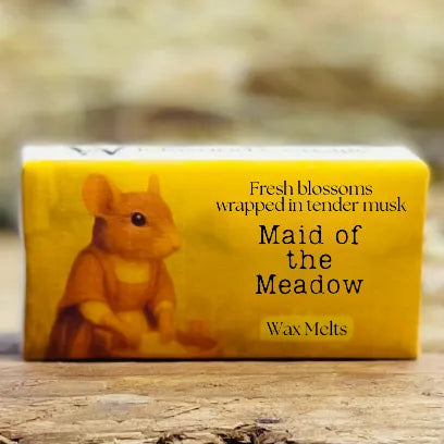 A close-up of the “Maid of the Meadow” wax melt packaging with soft floral meadow hues.