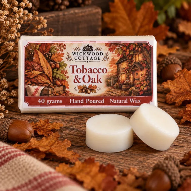Wickwood Cottage Tobacco & Oak 40g natural wax melts, featuring two ivory wax discs beside their autumn-inspired packaging on a rustic wooden table, surrounded by oak leaves, acorns and warm cottage lighting.