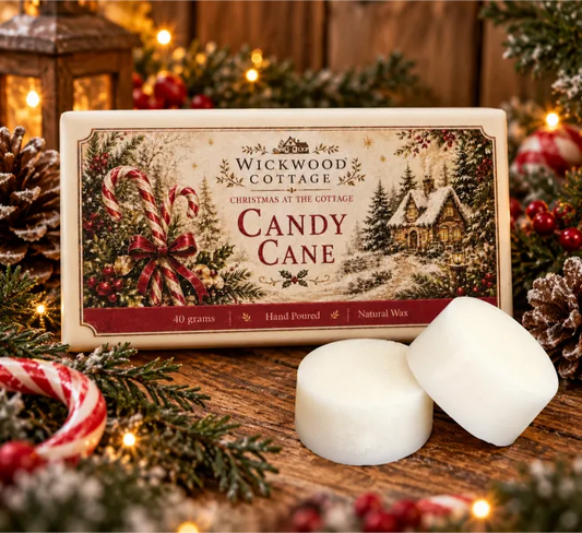 Wickwood Cottage Candy Cane 40g hand-poured natural wax melts, featuring two chunky ivory wax discs beside festive cottage-inspired packaging on a rustic wooden table, surrounded by red and white candy canes, frosted evergreen branches, pinecones, winter berries and warm Christmas fairy lights.