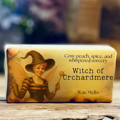 A close-up of the “Witch of Orchardmere” wax melt packaging with warm peach and spice tones.