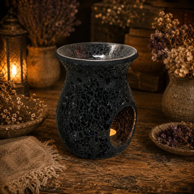 A dark, textured ceramic wax warmer with a crackle glaze and a cutout for a tea light, styled on a rustic wooden table with dried flowers and warm lanterns in the background.