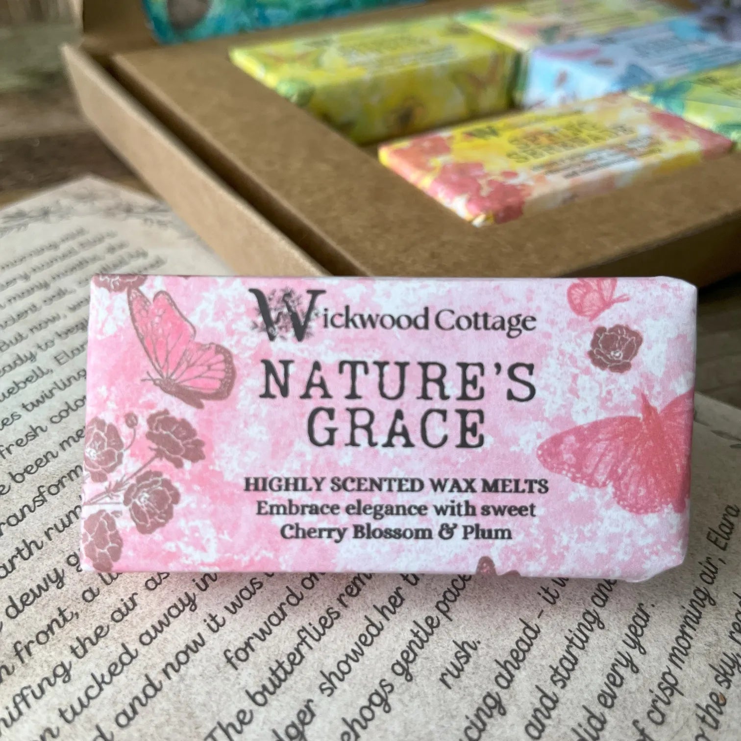 Paper packaging of Wickwood Cottage Nature's Grace highly scented wax melts. The packaging has a floral pattern with pink background and informative text. In the background is the gift box. Underneath is the story which comes with the gift box.
